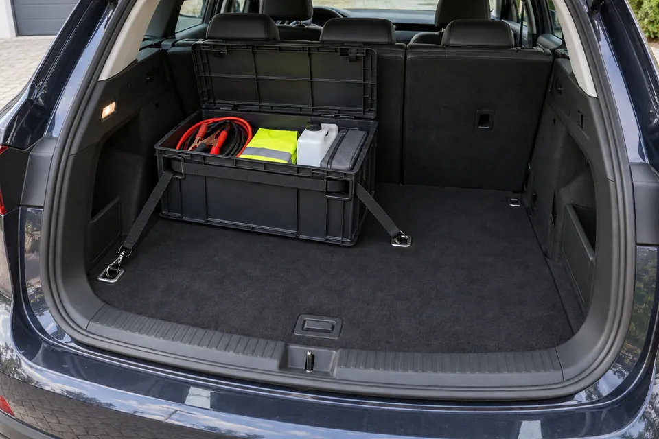 Caisse de rangement rigide noire à couvercle ouvert dans le coffre d’un SUV, contenant câbles de démarrage, gilet, bidon de lave-glace et trousse à outils, retenue par une sangle aux anneaux d’arrimage